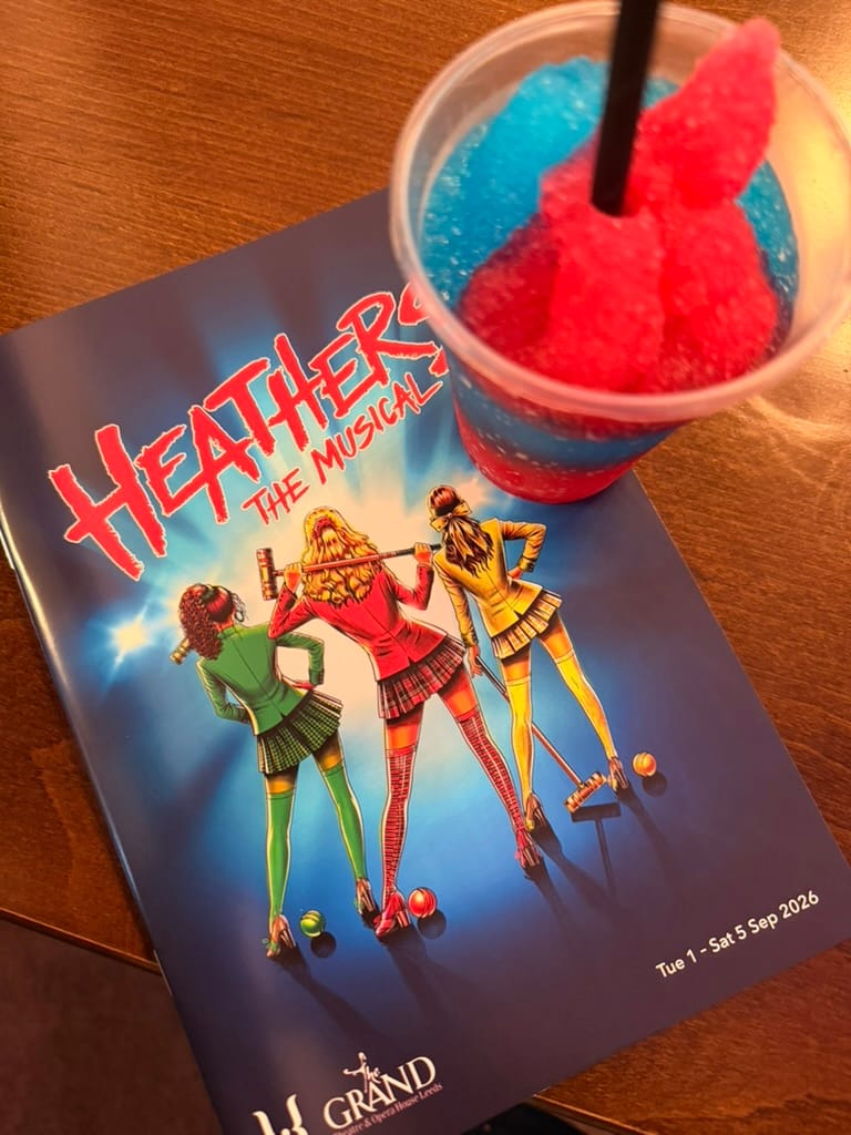 Heathers the Musical programme at Leeds Grand Theatre alongside a red and blue frozen drink