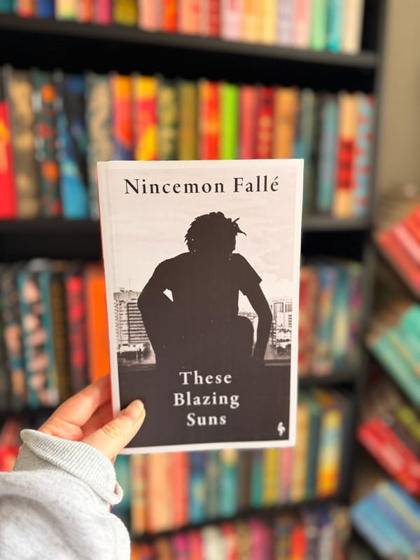 A hand holding a copy of These Blazing Suns by Nincemon Fallé.